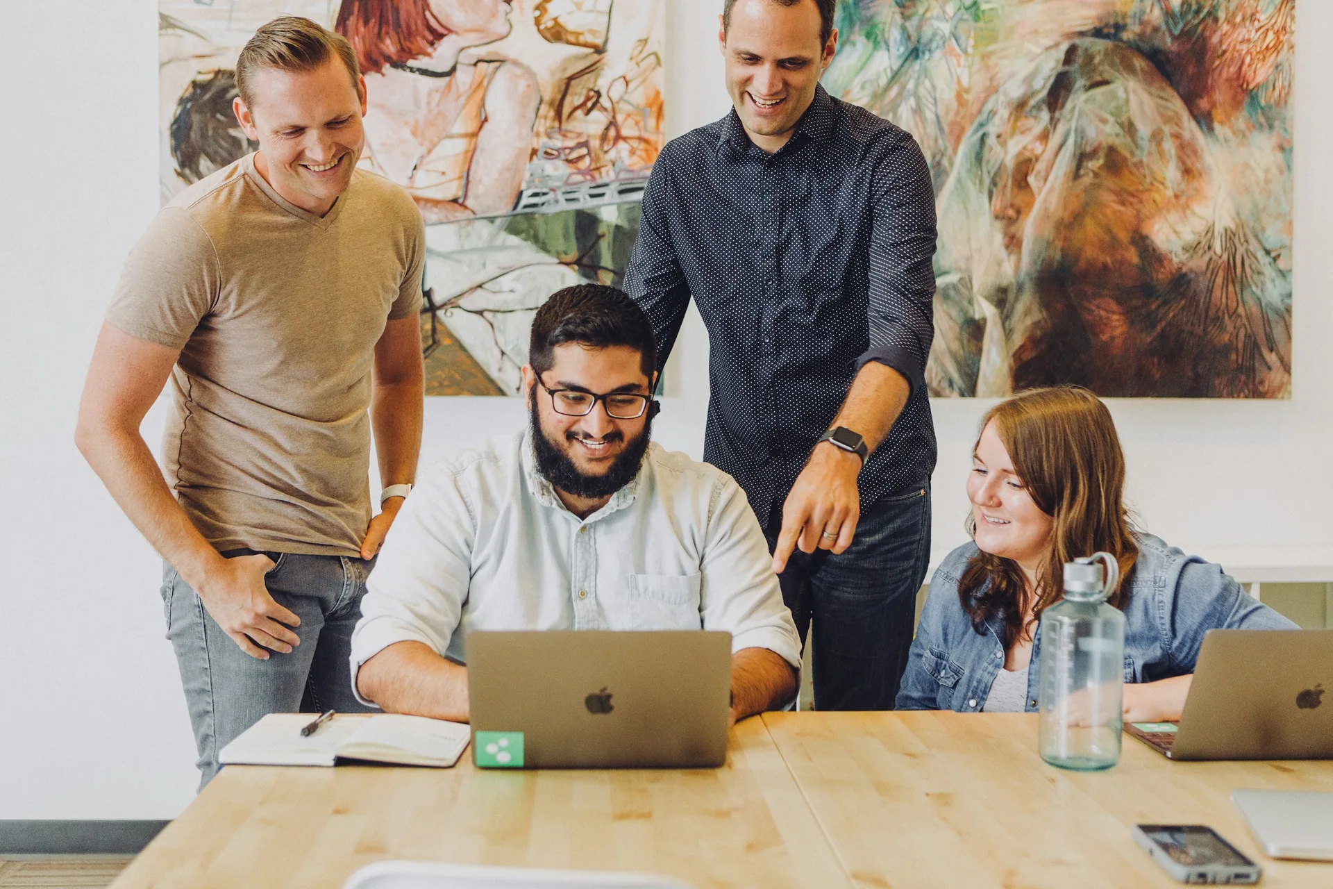 Four colleagues talk around a laptop in an office with natural light